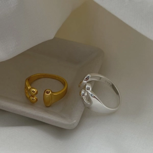 Asymmetric water drop rings in silver and gold colors on a minimalist ceramic tray