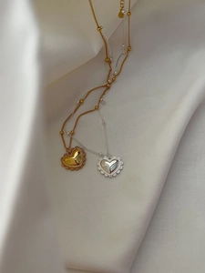 Détail des pendentifs cœur avec bords perlés en or et argent sur fond de soie