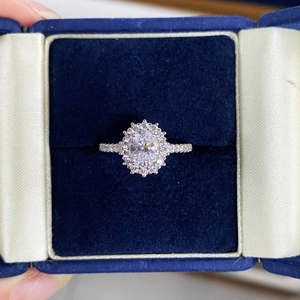 Macro view of oval cut halo gemstone ring with shimmering side diamonds in a blue velvet box