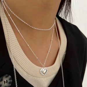 Collier à pendentif cœur argenté avec chaînes superposées et texture sur un mannequin