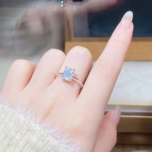 Detail of emerald cut moissanite ring on finger showing the classic four-prong setting