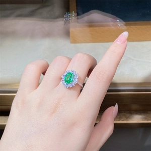 Close-up of a silver ring featuring an oval green gemstone and diamond halo on a finger