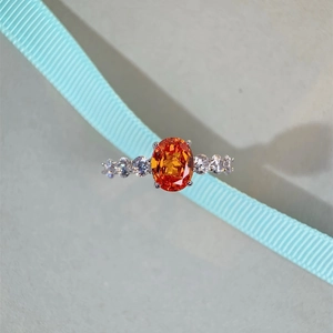 Detail of s925 silver ring with oval orange gemstone and small white zircons on blue ribbon