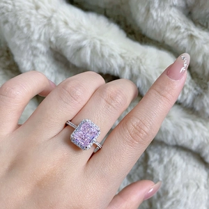 Macro shot of a rectangular pink radiant cut halo ring on a soft white plush background