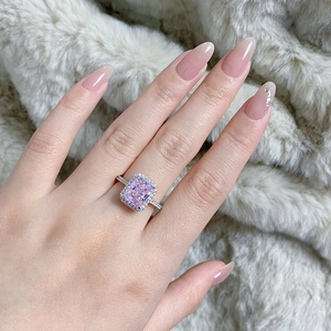 Detailed view of pink rectangular halo ring with diamond-encrusted band on model hand
