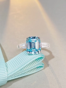 Macro shot of 6-carat emerald-cut aquamarine zircon ring with silver three-stone setting