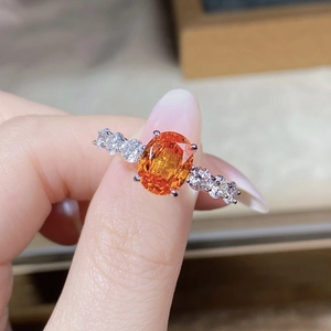 Macro shot of oval orange gemstone ring with sparkling side zircons in silver setting