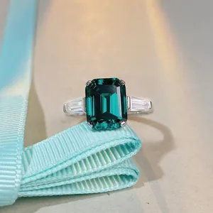 Macro view of emerald-cut green gemstone ring with baguette diamonds on blue ribbon