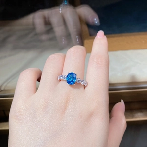 Detailed close-up of oval blue sapphire silver ring with white zircon side stones on hand