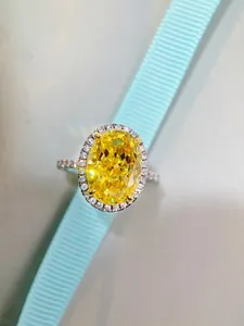 Détail macro d'une bague avec gemme jaune ovale et halo de diamants sur ruban bleu