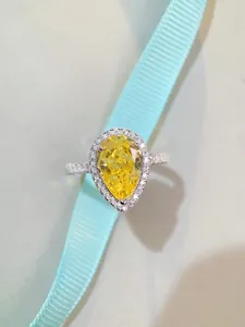 Detailed view of pear cut yellow gemstone ring with diamond halo and ribbon background