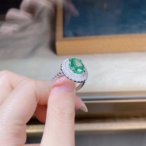 Dettaglio di un anello con pietra verde ovale e doppia aureola di diamanti scintillanti