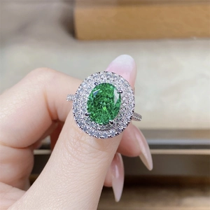 Dettaglio anello con gemma verde ovale e doppia corona di diamanti bianchi