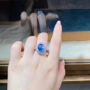 Macro shot of oval blue sapphire ring with double halo diamond setting on hand