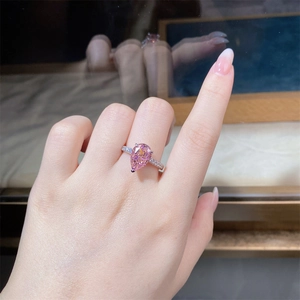 Close-up of a pear-cut pink stone ring with sparkling side stones on a finger