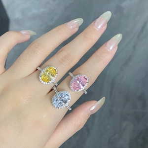 Détail de bagues halo avec pierres ovales jaunes, roses et blanches portées à la main