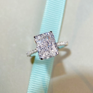 Radiant cut silver ring with pavé diamond band on a blue ribbon background