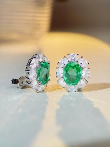 Macro shot of silver stud earrings with oval emerald-green stones and zircon halo