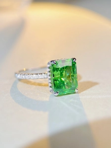 Macro detail of emerald-cut green gemstone ring with pavé-set diamonds on silver band