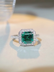 Macro shot of emerald-cut green stone with halo setting and pavé-set silver band