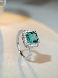 Macro detail of emerald-cut green gemstone ring with halo diamond setting in silver