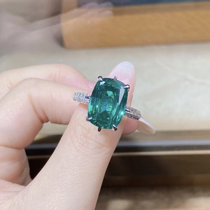 Vista macro di un anello con pietra preziosa verde smeraldo taglio cushion e pavé di diamanti