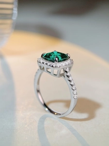 Macro shot of an emerald-cut green stone ring with halo diamonds on a silver band