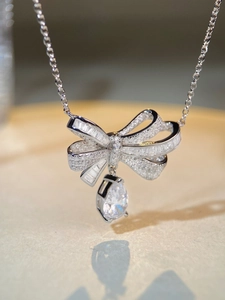 Macro shot of silver bow pendant with baguette diamonds and pear-shaped drop