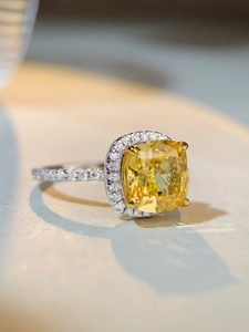 Gros plan d'une bague avec gemme jaune coupe coussin et halo de diamants pave