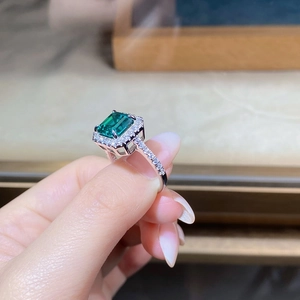Macro detail of emerald-cut green gemstone with brilliant halo setting on silver ring