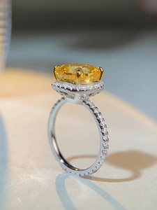 Détail d'une bague avec gemme jaune coupe radiant, halo de diamants et anneau pavé argent