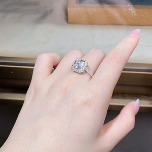 Gros plan d'une bague à coupe émeraude avec double halo serti sur le doigt d'une femme