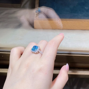 Macro shot of rectangular blue stone ring with halo pavé setting on a model finger
