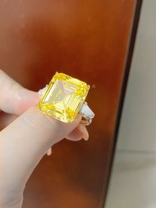 Macro shot of 28ct emerald cut yellow gemstone ring on hand with silver side stones