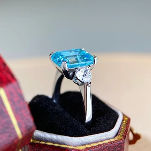 Macro shot of 4 carat emerald-cut blue gemstone ring with heart side stones in red box