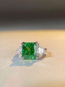 Macro shot of large square emerald-cut green gemstone ring with side triangular stones