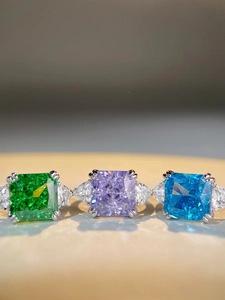 Detailed view of three-stone silver rings with square cut emerald, violet and blue gems