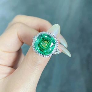 Macro shot of halo setting emerald green stone ring on hand with sparkling side diamonds