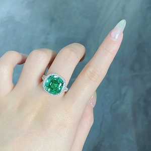 Close-up of cushion-cut green gemstone ring with halo diamond setting on woman's hand