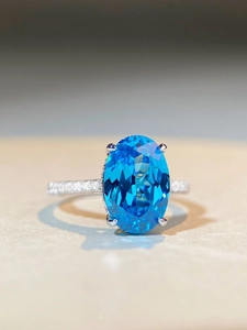 Macro detail of oval cut blue gemstone ring with sparkling micro-paved diamond band