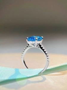 Macro view of oval-cut blue gemstone ring with micro-pave diamond accents in silver