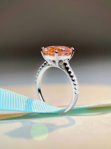 Macro side view of silver ring with oval orange gemstone and pavé diamond band details