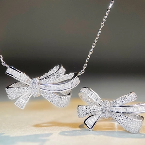 Macro shot of silver bow jewelry set featuring pavé diamonds on necklace and ring