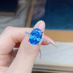 Close-up of a large oval-cut blue gemstone ring featuring micro-pave diamond accents