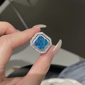 Close-up of radiant cut aquamarine blue square ring with double diamond halo on finger