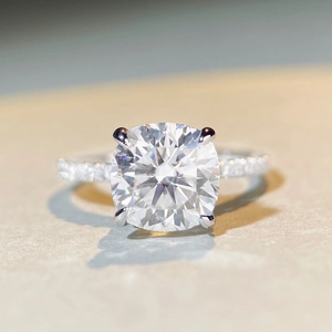 Macro view of cushion-cut moissanite ring with pavé-set silver band on neutral surface