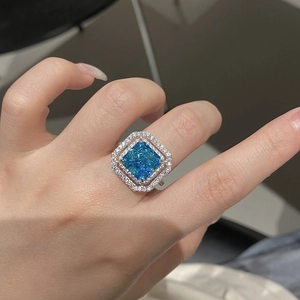 Close-up of a radiant cut blue gemstone ring with double halo pavé diamonds on hand