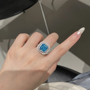 Close-up of radiant cut aquamarine silver ring with double layer halo diamonds on hand