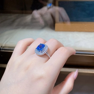 Close-up of blue cushion-cut ring with double halo pavé diamonds on finger