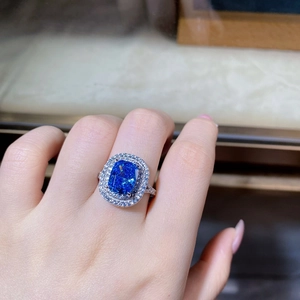 Close-up of a blue square-cut gemstone ring with a double halo and pavé band